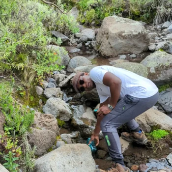 a man in a white shirt and sunglasses bending over a stream of rocks